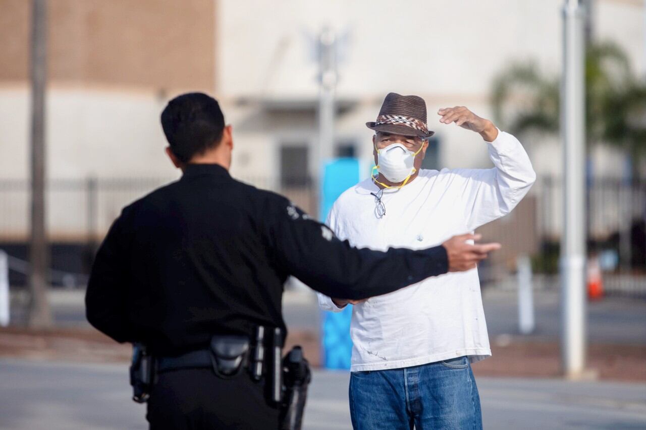 Un oficial de policía conversa con un hombre que lleva una mascarilla como medida preventiva contra el coronavirus. Imagen referencial en el Puerto de Los Ángeles en San Pedro, California. (AFP / Apu GOMES).