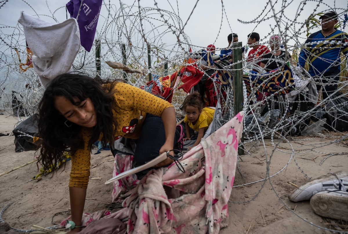 Migrantes se arrastran para cruzar a través de un agujero en el alambre de púas en Texas (Foto de ANDREW CABALLERO-REYNOLDS / AFP).
