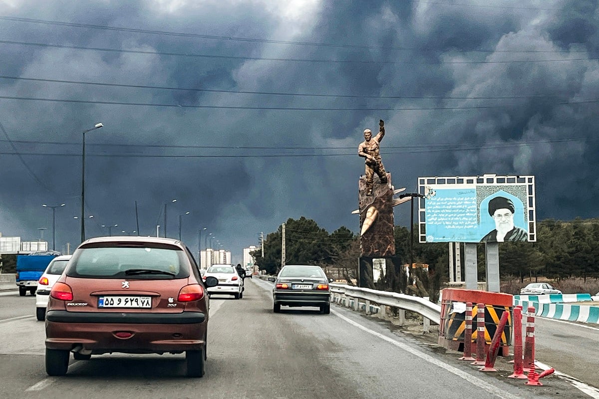 Vehículos circulan por una autopista, con columnas de humo negro elevándose, en Teherán, Irán, el 8 de marzo de 2026. (AFP)