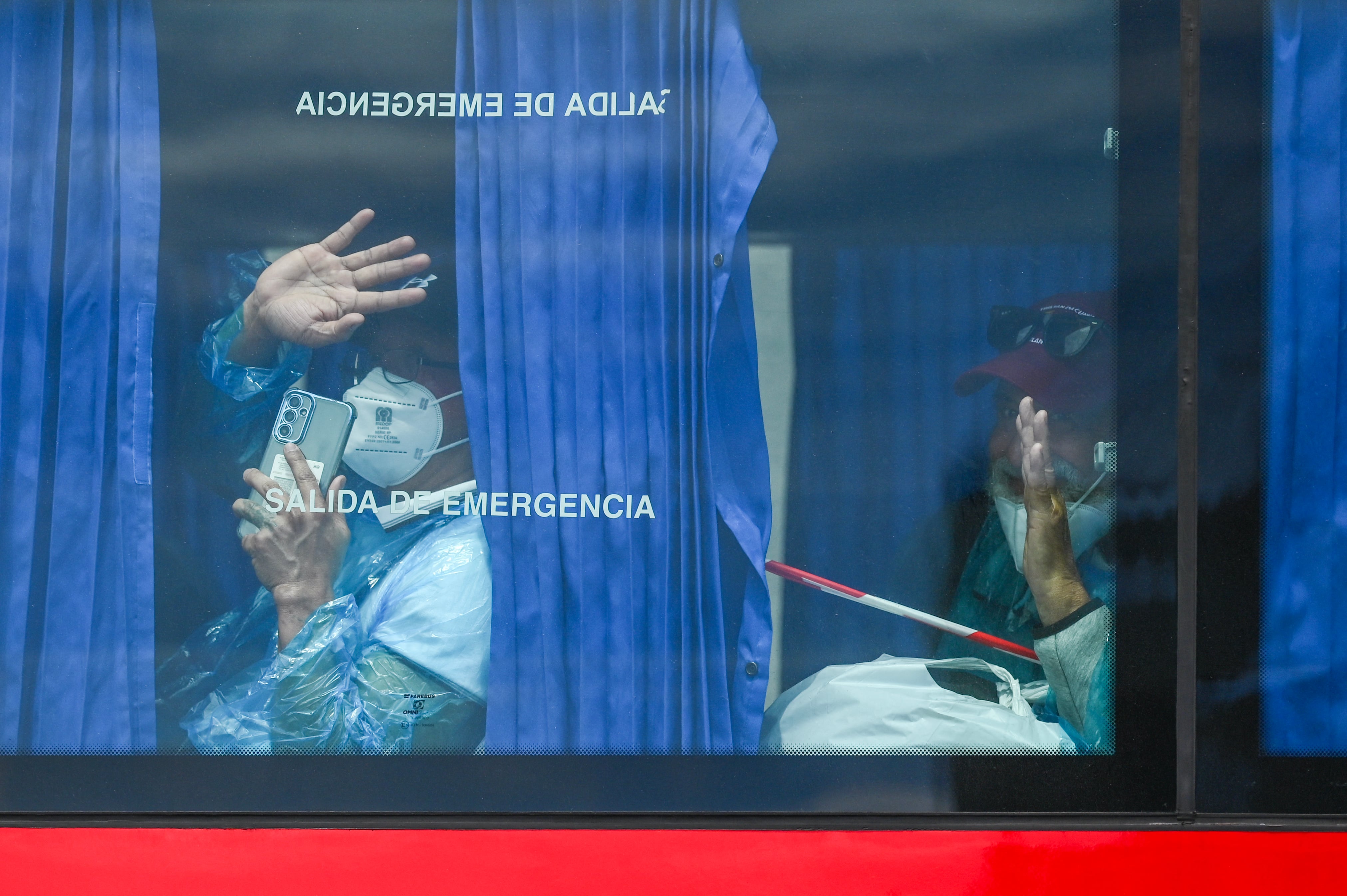 Pasajeros evacuados del crucero MV Hondius, con bandera holandesa y afectado por el hantavirus, saludan a bordo de un autobús militar tras ser trasladados en barco al puerto industrial de Granadilla de Abona. (Foto de JORGE GUERRERO / AFP).