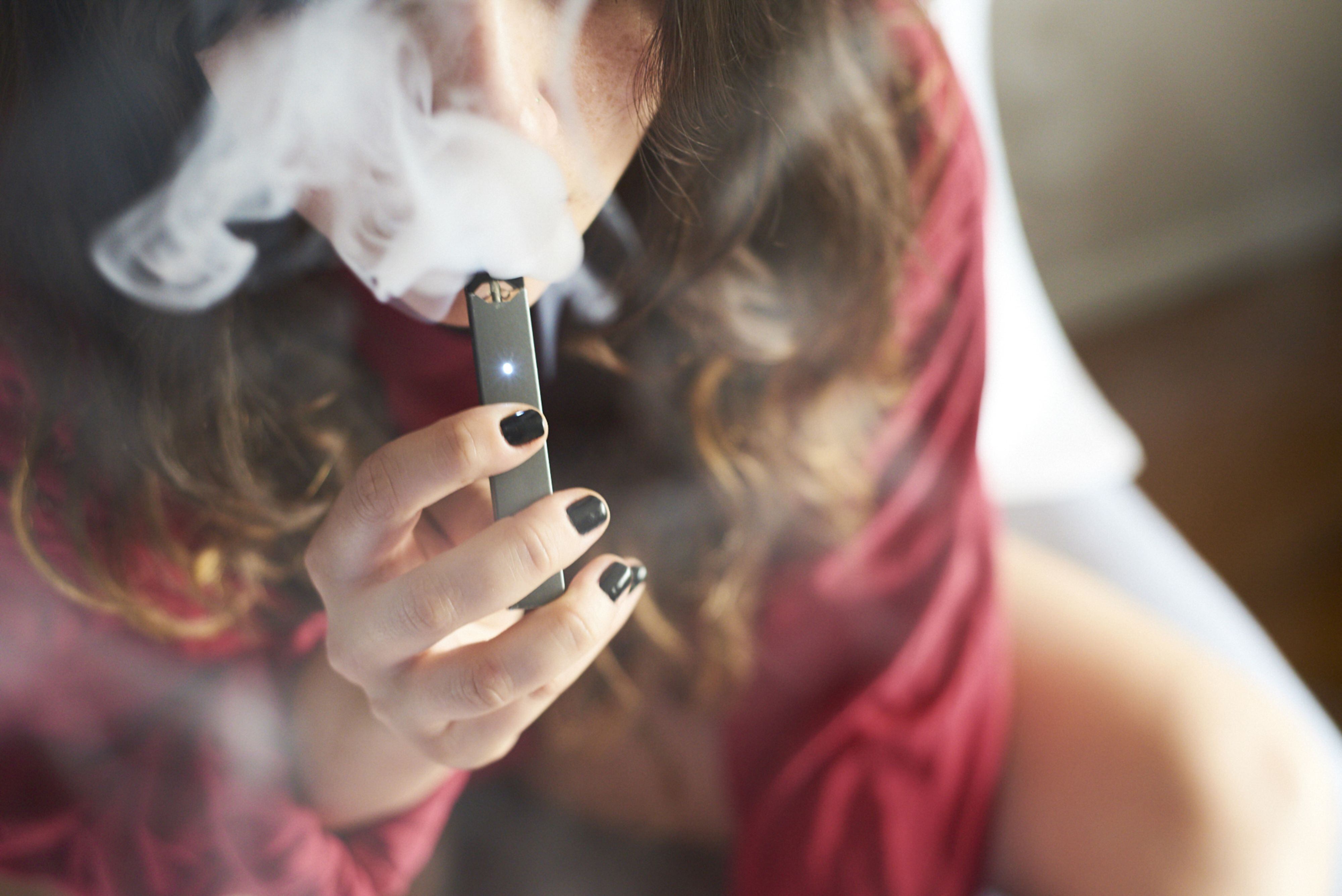 A person smokes a Juul Labs Inc. e-cigarette in this arranged photograph taken in the Brooklyn Borough of New York, U.S., on Sunday July 8, 2018. Juul Labs, the maker of the popular e-cigarette brand that has recently come under fire from health officials over its popularity with young adults, plans to introduce a line of lower-nicotine pods. The company will begin to sell pods with a 3-percent nicotine concentration in its mint and Virginia tobacco flavors later this year, according to a statement Thursday.