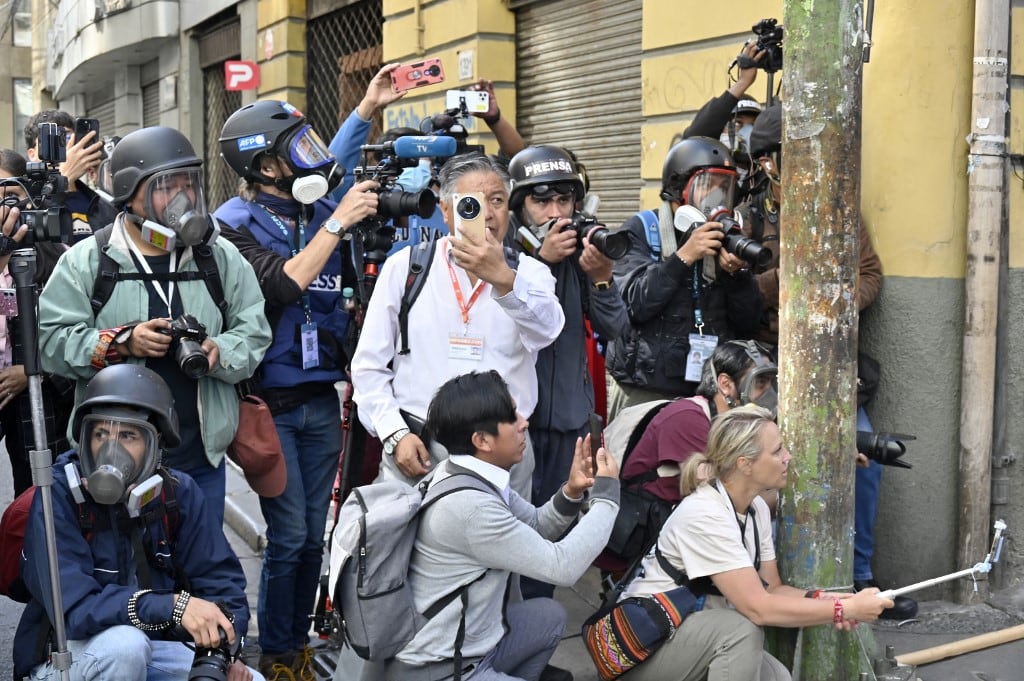 Miembros de los medios de comunicación trabajan mientras la policía antidisturbios se enfrenta a manifestantes durante una protesta que exige la renuncia del presidente boliviano Rodrigo Paz, en La Paz, el 18 de mayo de 2026. (Foto de Aizar RALDES / AFP)