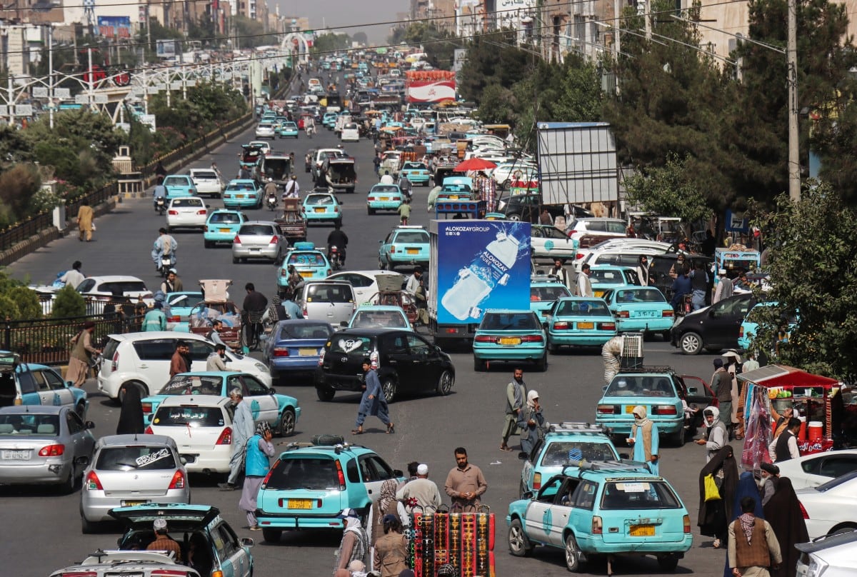 Esta fotografía, tomada el 1 de julio de 2026, muestra a personas desplazándose en taxis azules en una plaza de Herat. (Photo by Mohsen KARIMI / AFP)