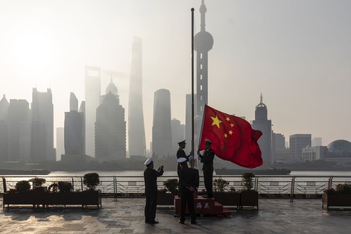 China Customs officers raise a Chinese flag during a rehearsal for a flag-raising ceremony along the Bund in front of buildings in the Lujiazui Financial District at sunrise in Shanghai, China, on Tuesday, Jan. 4, 2022. A wall of maturing debt and a surge in seasonal demand for cash will test Chinas financial markets this month, putting pressure on the central bank to ensure sufficient liquidity. Photographer: Qilai Shen/Bloomberg