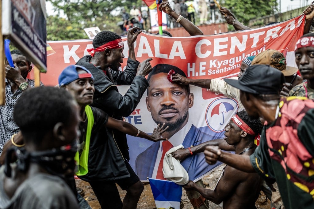 Partidarios del líder de la oposición ugandesa y candidato presidencial de la Plataforma de Unidad Nacional (PNU), Robert Kyagulanyi Ssentamu, conocido popularmente como Bobi Wine, corean consignas mientras sostienen una bandera con su rostro durante el último mitin de campaña del partido antes de las elecciones generales de 2026, en Kampala el 12 de enero de 2026. (Foto de Luis TATO / AFP)