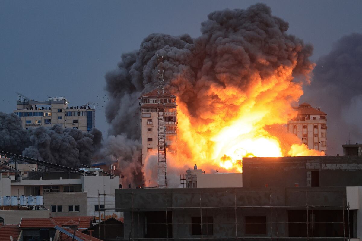 Personas paradas en una azotea observan cómo una bola de fuego y humo se eleva sobre un edificio en la ciudad de Gaza el 7 de octubre de 2023 durante un ataque aéreo israelí. (Foto de MAHMUD HAMS / AFP)