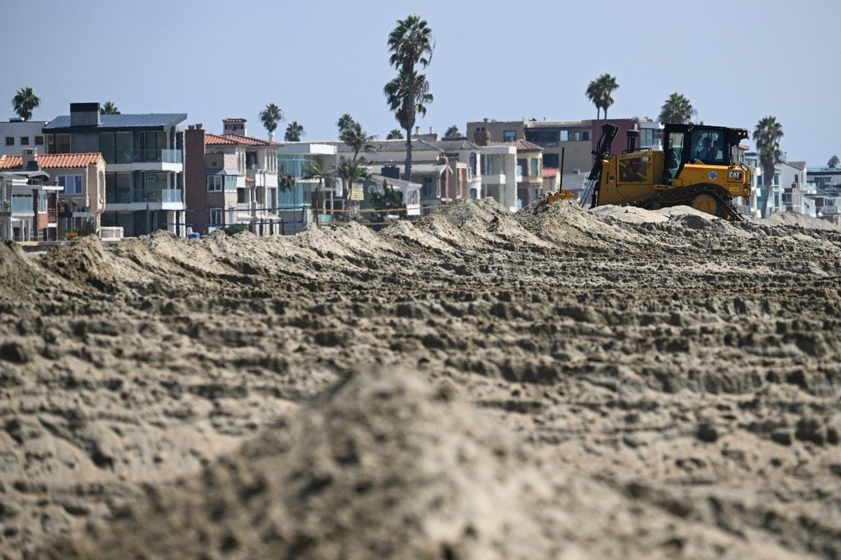 Una excavadora construye un muro de contención de arena para proteger las viviendas, mientras los trabajadores se preparan ante el fuerte oleaje, las inundaciones costeras y la erosión de las playas que traerá consigo el huracán Polo en Long Beach, California, el 24 de septiembre de 2026 (Foto: Patrick T. Fallon / AFP)