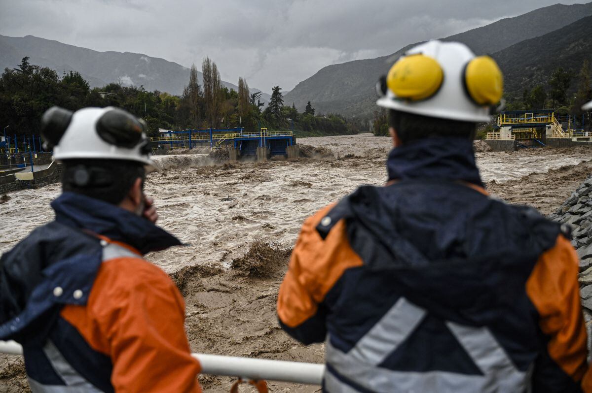Técnicos de la empresa Aguas Andinas observan una presa de captación de agua en el río Maipo en San José de Maipo, Santiago, Chile, el 23 de junio de 2023. Las fuertes lluvias están afectando la zona central de Chile, provocando que varios ríos se desborden (Foto: Martín Bernetti / AFP)