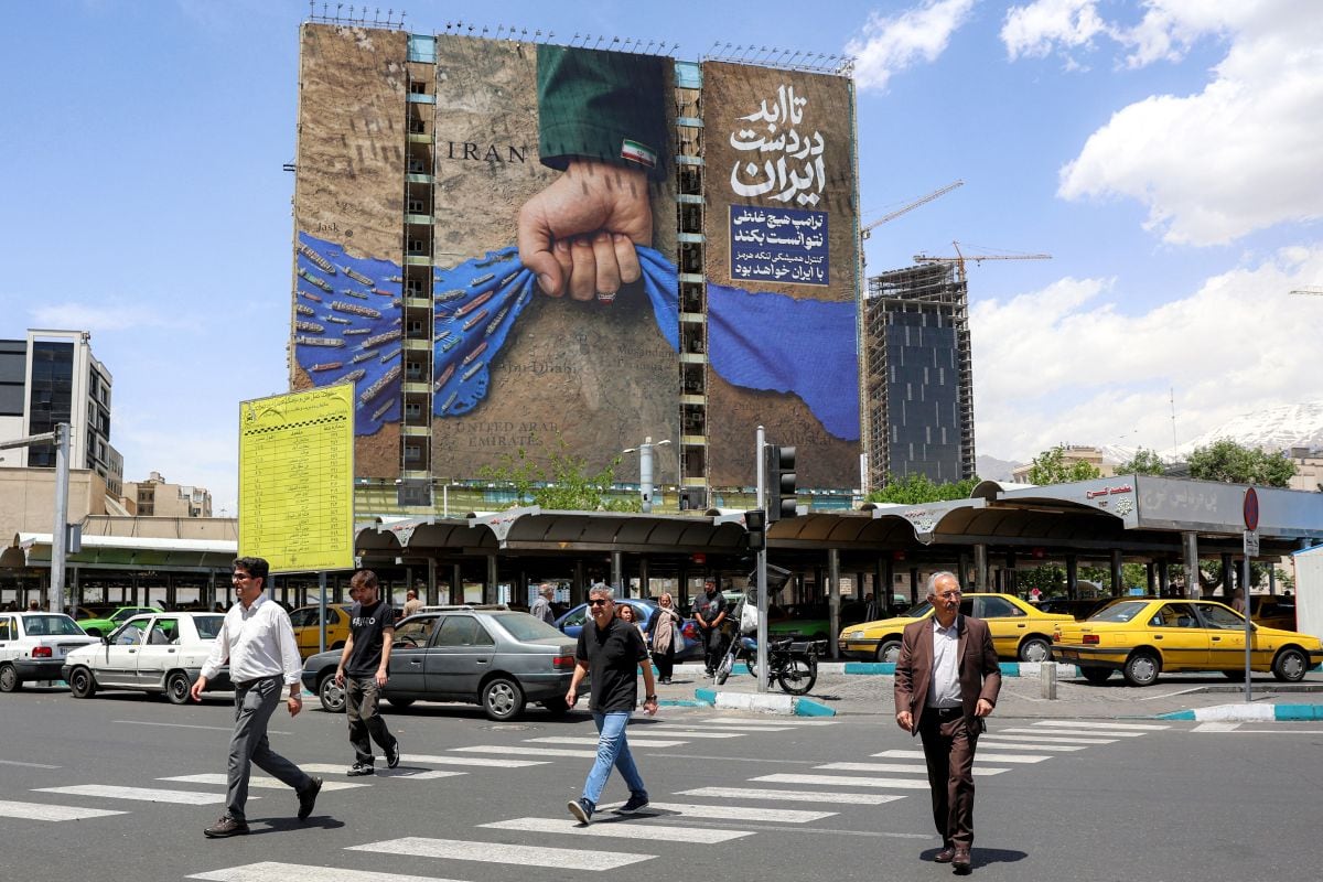Varias personas cruzan una calle cerca de una valla publicitaria situada en la fachada de un edificio que muestra el estrecho de Ormuz con un letrero en persa que reza «Para siempre en manos de Irán», en la plaza Vanak de Teherán, el 6 de mayo de 2026. Foto: AFP