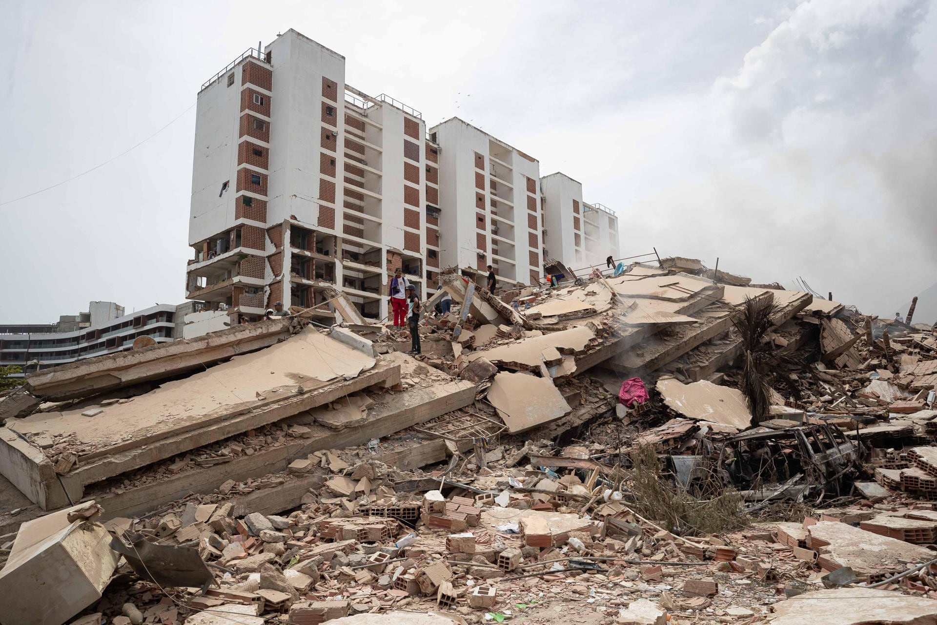 Personas caminan por escombros de edificios afectados por terremotos en La Guaira, Venezuela. (EFE/ Ronald Peña R.).