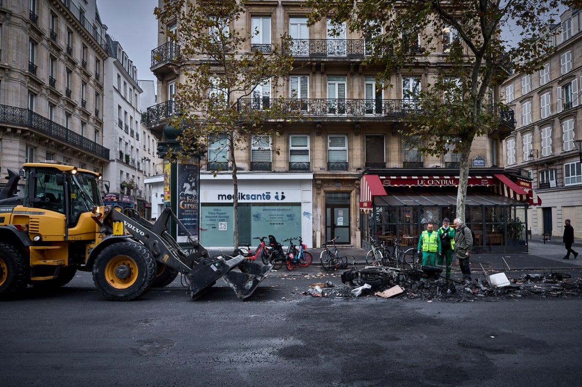 Municipal workers and a member of the public look at the burnt out remains of a barricade on Boulevard de Sebastapol during a clean up of the capital after a weekend of protests against the "high cost of living", in central Paris on October 19, 2026. France's Prime Minister said 1,200 people were arrested in protests across the country on October 17, and 150 police were hurt during clashes between police and protesters. Massive looting and multiple blazes gripped France as nationwide marches against soaring inflation degenerated into street violence of "extreme intensity". (Photo by Kiran RIDLEY / AFP)