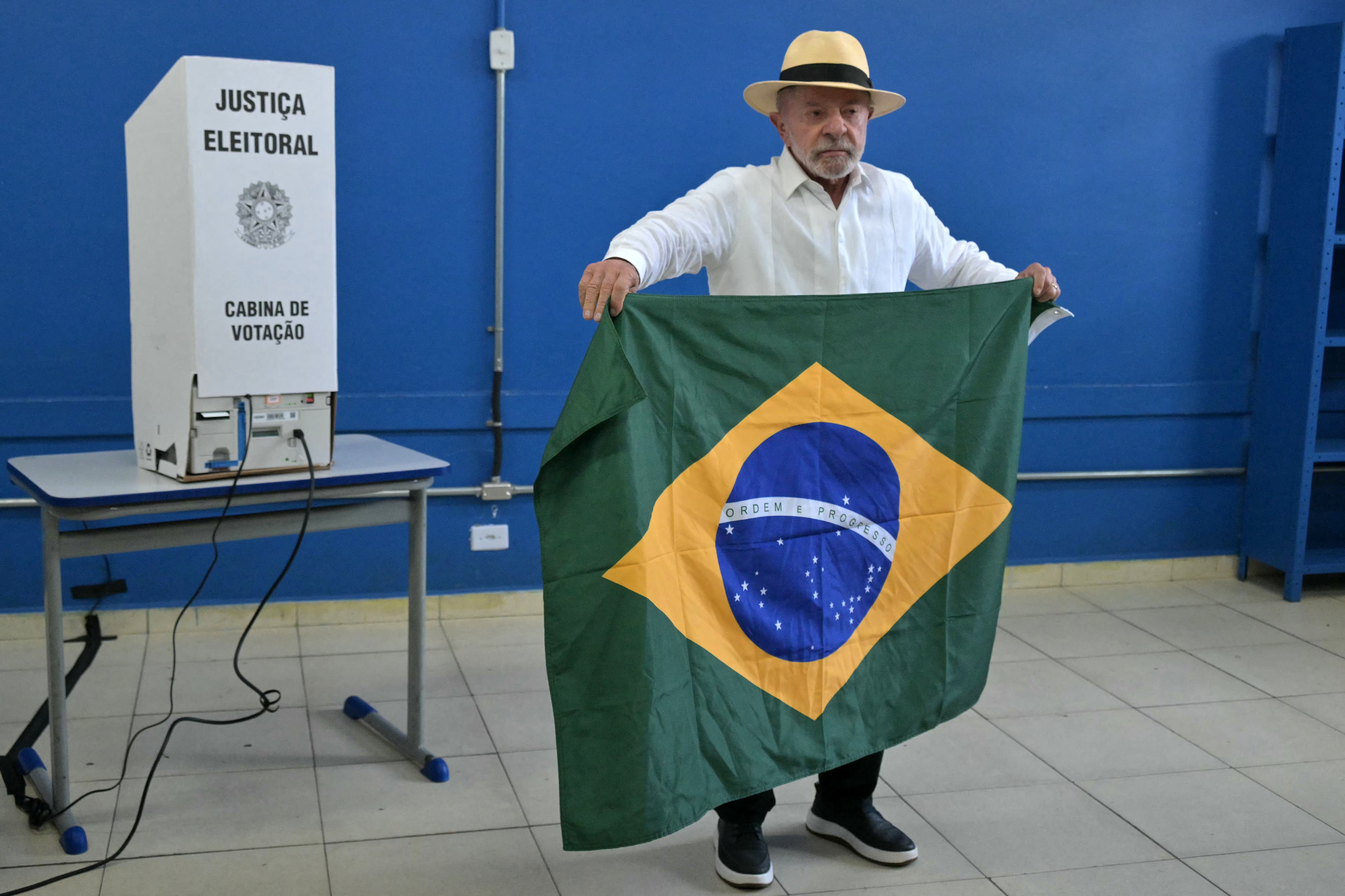 El presidente de Brasil y candidato a la reelección por el Partido de los Trabajadores (PT), Luiz Inácio Lula da Silva, sostiene una bandera brasileña mientras vota en São Paulo. (Foto de NELSON ALMEIDA / AFP).