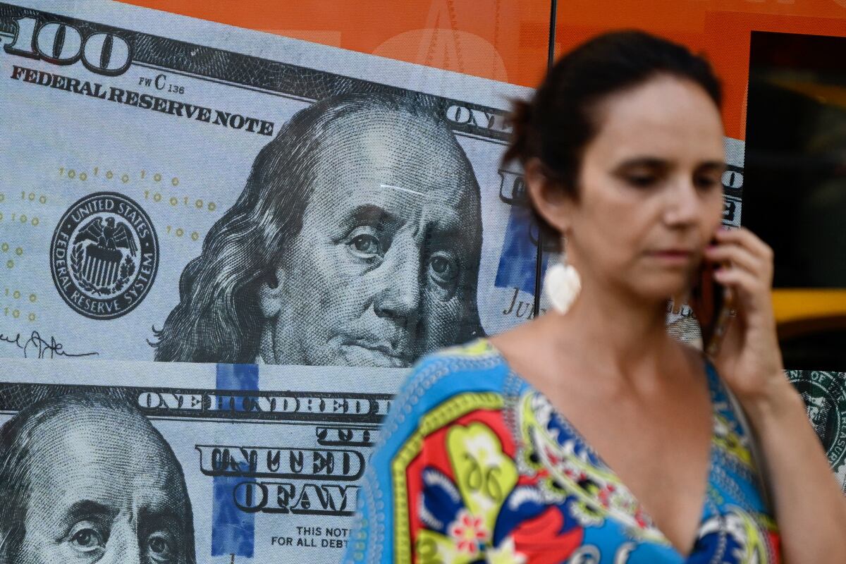 Una mujer pasa junto a una imagen de billetes de dólares estadounidenses en Buenos Aires, Argentina, el 12 de diciembre de 2023 (Foto de Luis Robayo / AFP)