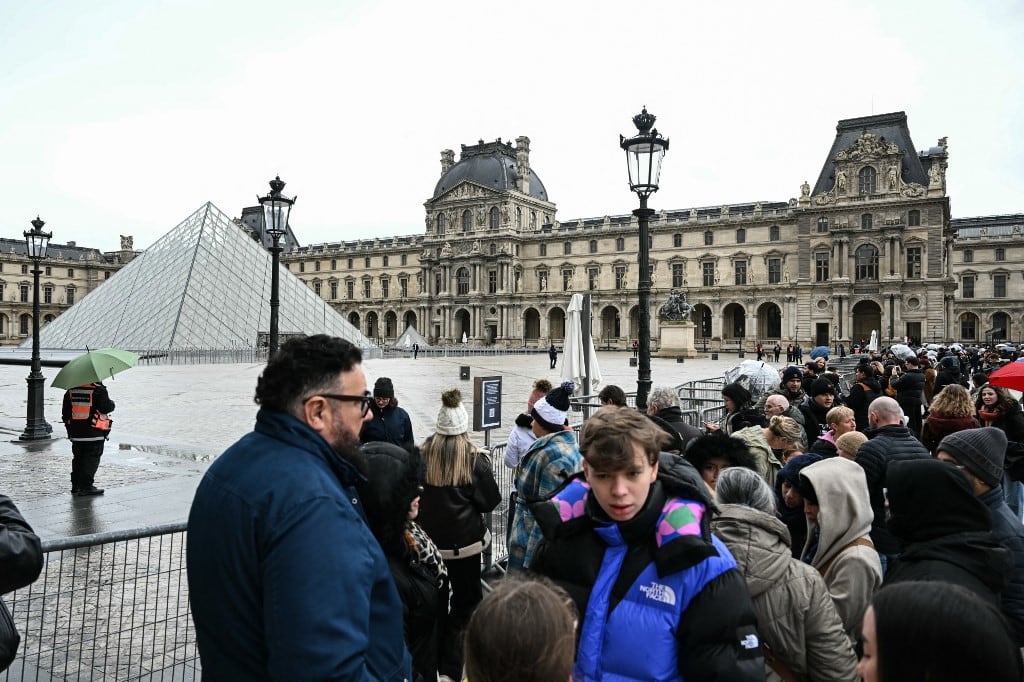 Turistas junto a las barreras que bloquean la plaza con la Pirámide del Louvre, diseñada por el arquitecto chino-estadounidense Ieoh Ming Pei, debido al cierre del Museo del Louvre debido a una huelga en París el 12 de enero de 2026. El museo se vio obligado a cerrar el 12 de enero de 2026 después de que su personal, en huelga desde mediados de diciembre para obtener mejores condiciones laborales, decidiera continuar con la huelga, según supo AFP a través del museo y los sindicatos. (Foto de Martin LELIEVRE / AFP)