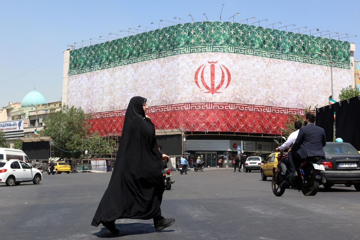 Una mujer iraní con velo pasa junto a una valla publicitaria con la bandera nacional de Irán en la plaza Enqelab de Teherán, Irán, el 14 de junio de 2026. Foto: EFE/EPA/ABEDIN TAHERKENAREH