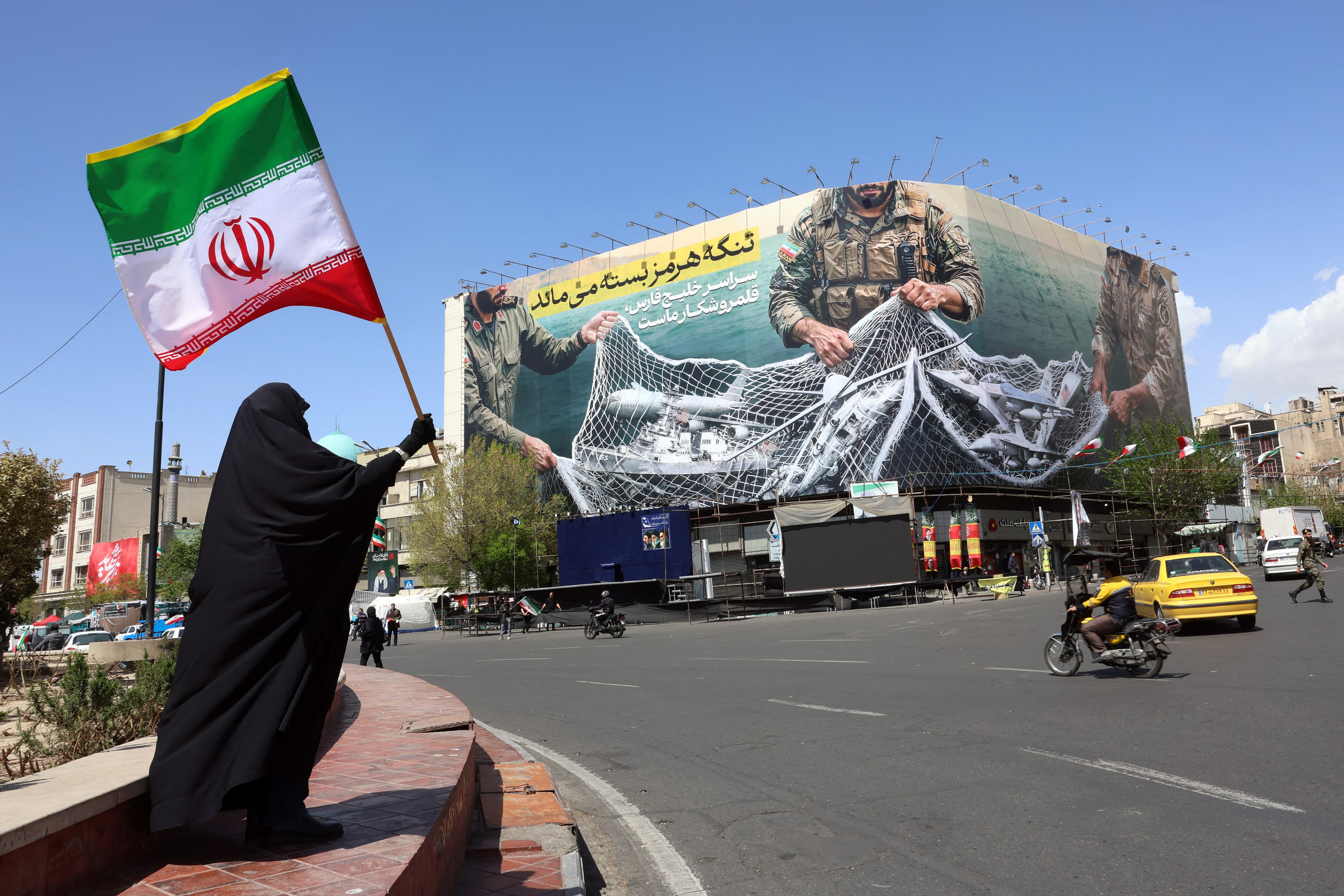 Una mujer sostiene la bandera de Irán mientras se encuentra cerca de una valla publicitaria con la frase "El estrecho de Ormuz permanece cerrado", el 5 de abril de 2026. (Foto de AFP).