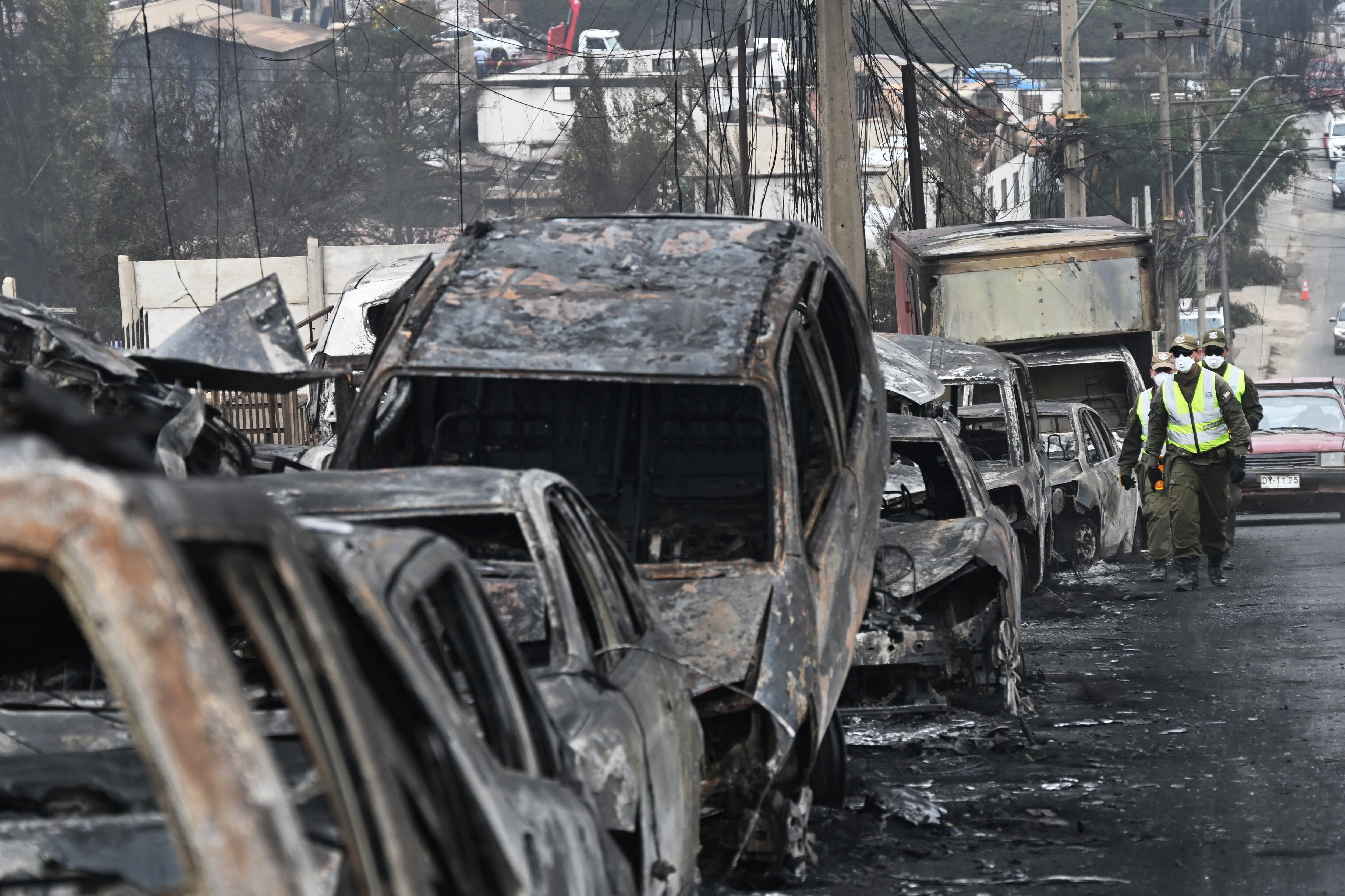 Carabineros chilenos pasan junto a vehículos quemados después de un incendio forestal en Quilpue, Viña del Mar, Chile, el 4 de febrero de 2024. (Foto de RODRIGO ARANGUA/AFP).