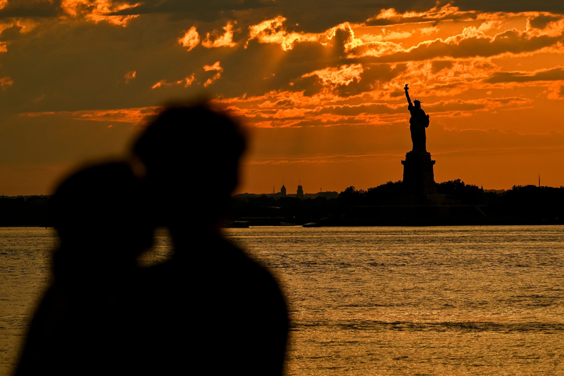 Una pareja disfrutando del sunset a través de la Estatua de la Libertad en Nueva York (Foto: AFP)