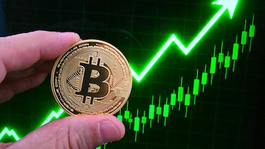 Ilustración de una moneda física de Bitcoin sostenida frente a un gráfico financiero con tendencia alcista en verde, tomada en París, Francia, el 5 de junio de 2026. (Foto de Joao Luiz Bulcao / Hans Lucas vía AFP).