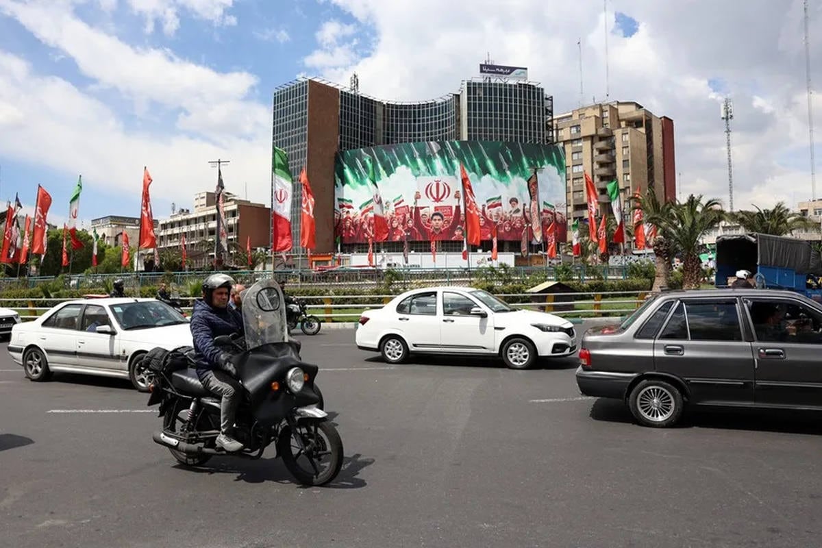 Ciudadanos iraníes pasan en coche junto a una gran valla publicitaria política con banderas nacionales de Irán en la plaza Valiasr de Teherán, Irán. (Foto: EFE)