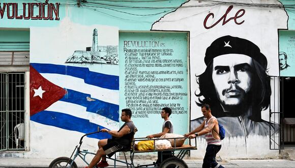 La gente transporta comida en un triciclo pasando junto a una pared pintada con la bandera de Cuba y un retrato del líder revolucionario argentino Ernesto "Che" Guevara, en La Habana. (Foto de YAMIL LAGE / AFP).