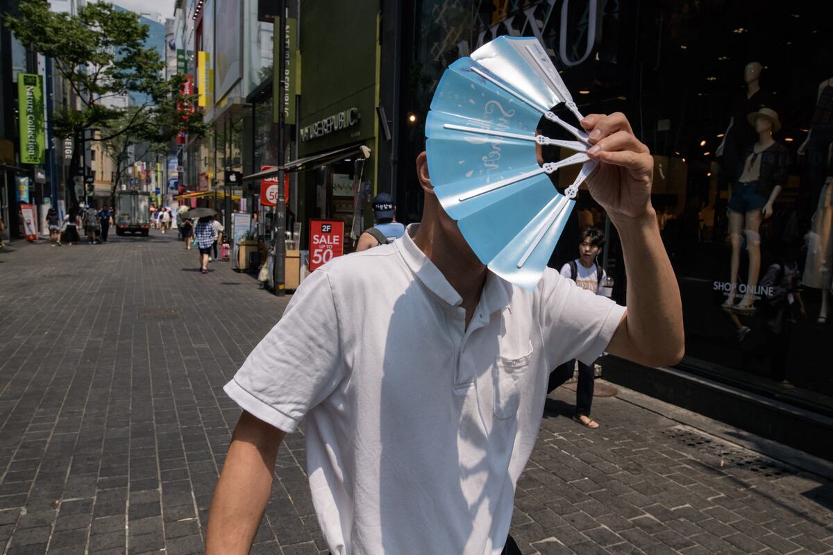 Imagen de archivo | Un hombre se protege la cara del sol mientras camina por el distrito comercial de Myeongdong en Seúl. (Foto de Ed JONES / AFP)