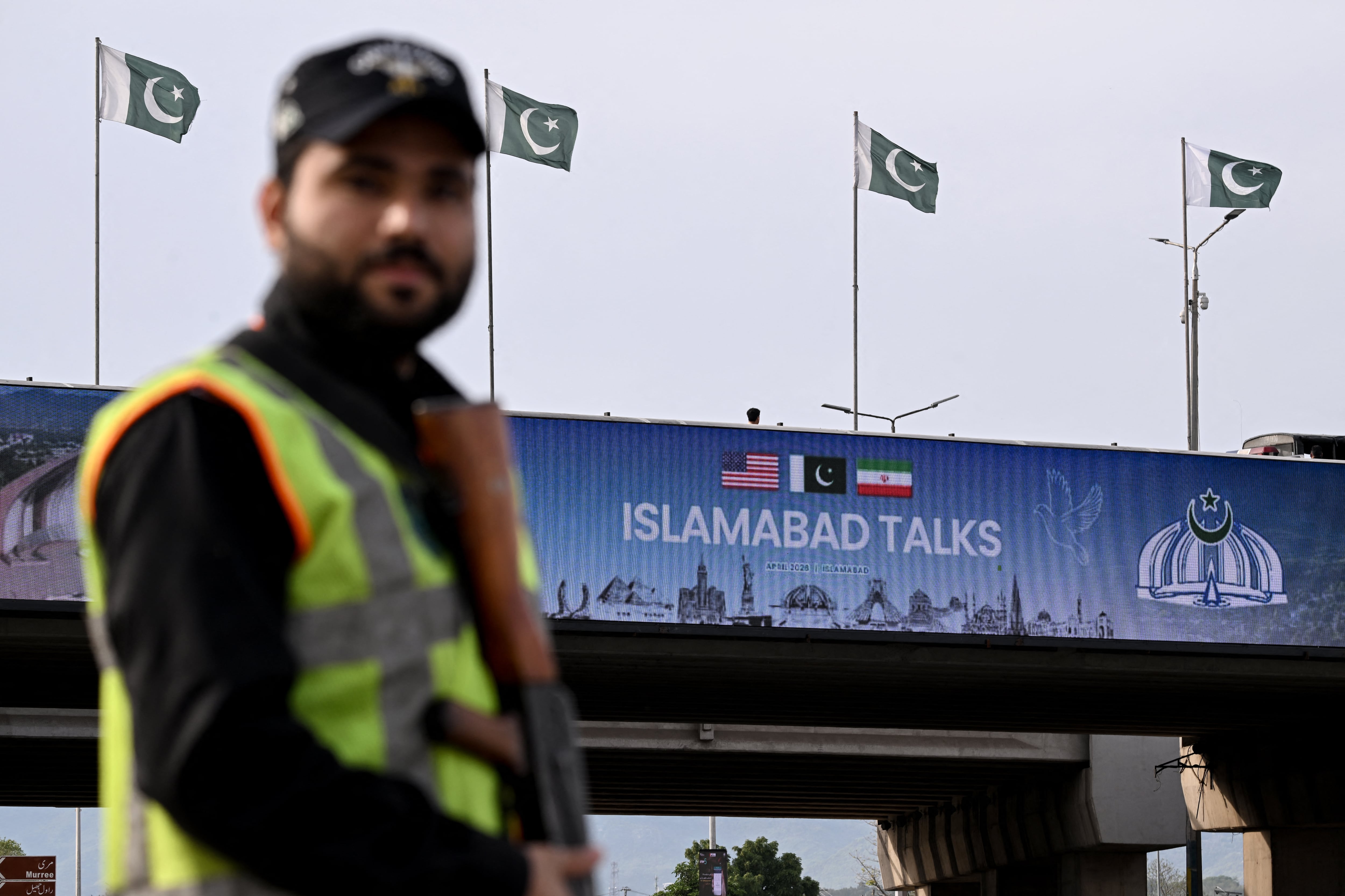 Un policía monta guardia frente a una pantalla digital que muestra noticias sobre las conversaciones de paz entre Estados Unidos e Irán en una calle de Islamabad el 10 de abril de 2026.(Foto de Farooq NAEEM / AFP).