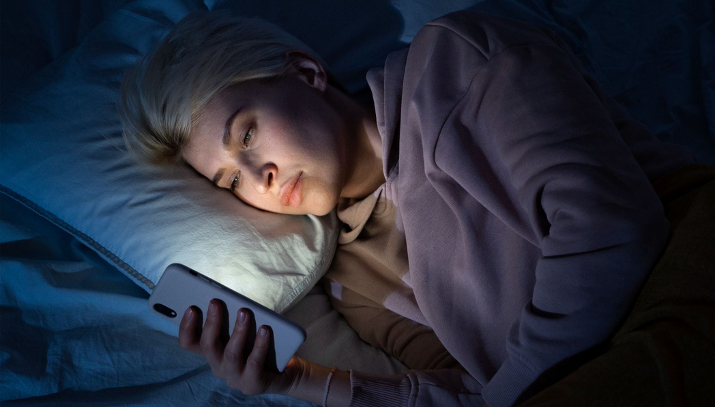 En esta imagen se puede apreciar a una mujer echada en su cama mientras mira su celular porque se le hace imposible dormir. (Foto: freepik)