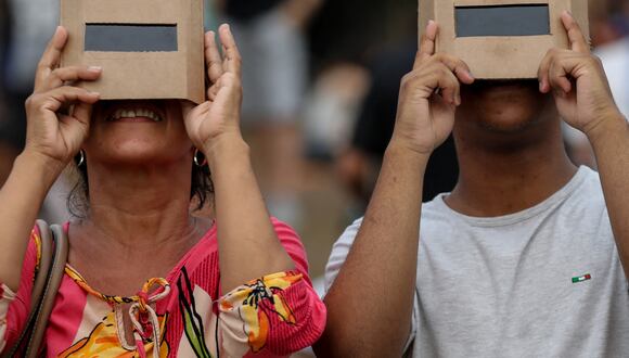 Dos personas protegiendo su vista con unos lentes especiales mientras observa un eclipse solar (Foto: AFP)