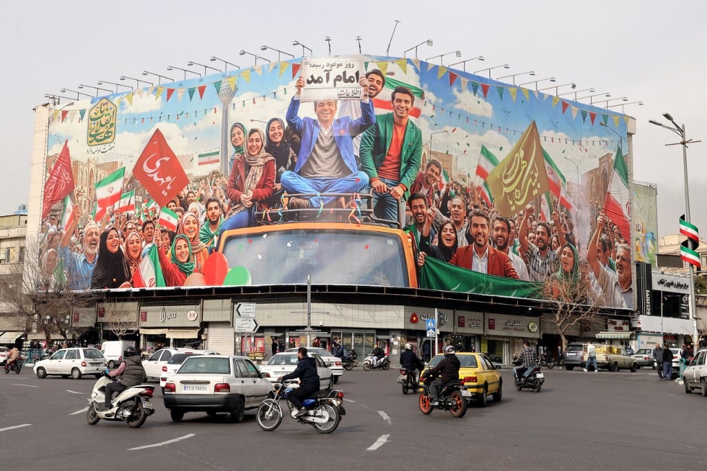 Los conductores pasan junto a una gran pancarta que muestra la imagen de la revolución victoriosa en Teherán el 3 de febrero de 2026, antes del 47.º aniversario de la Revolución Islámica de 1979. (Foto de ATTA KENARE / AFP)