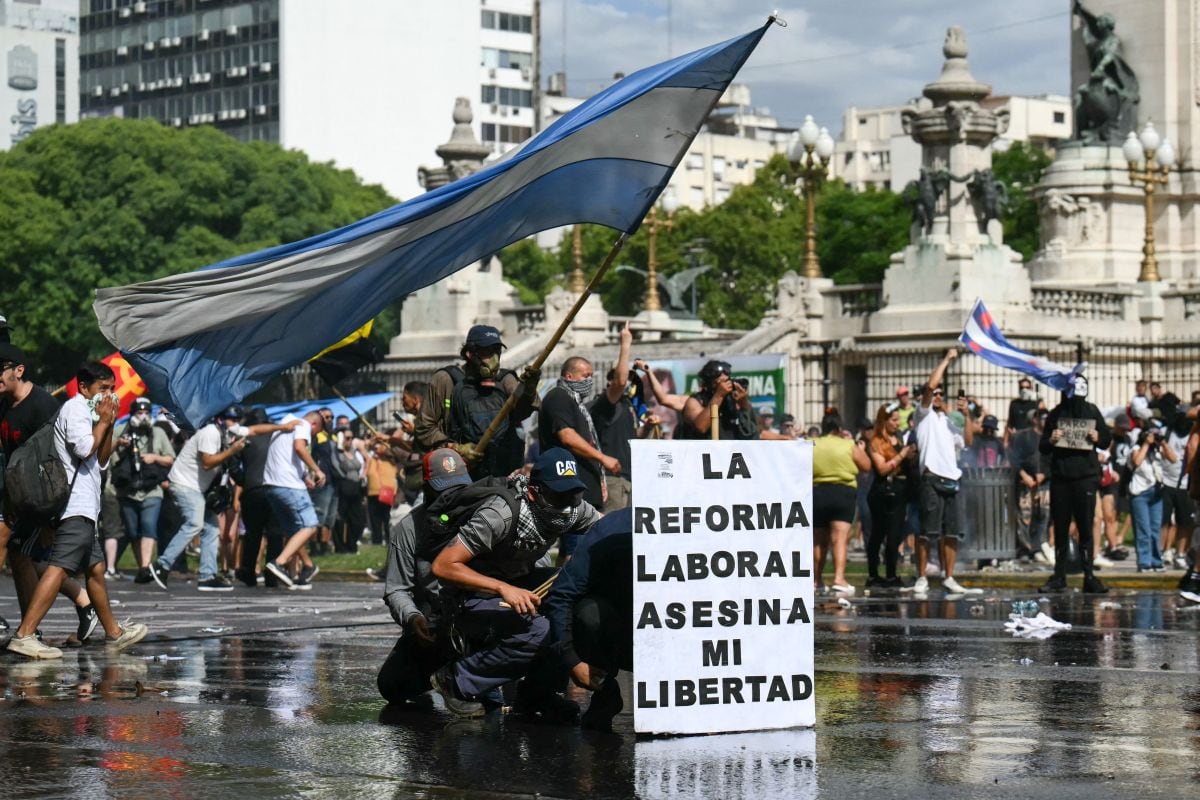 Manifestantes se protegen tras una pancarta que dice "La reforma laboral mata mi libertad" de un cañón de agua disparado por la policía antidisturbios durante una protesta convocada por sindicalistas contra el debate sobre la reforma laboral en el Congreso Nacional de Buenos Aires el 11 de febrero de 2026 (Foto: Luis Robayo / AFP)