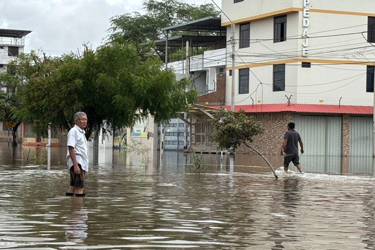 Vecinos caminan por una calle inundada en Piura, donde el agua cubre gran parte de la vía frente a viviendas y edificios. (Foto: GEC)