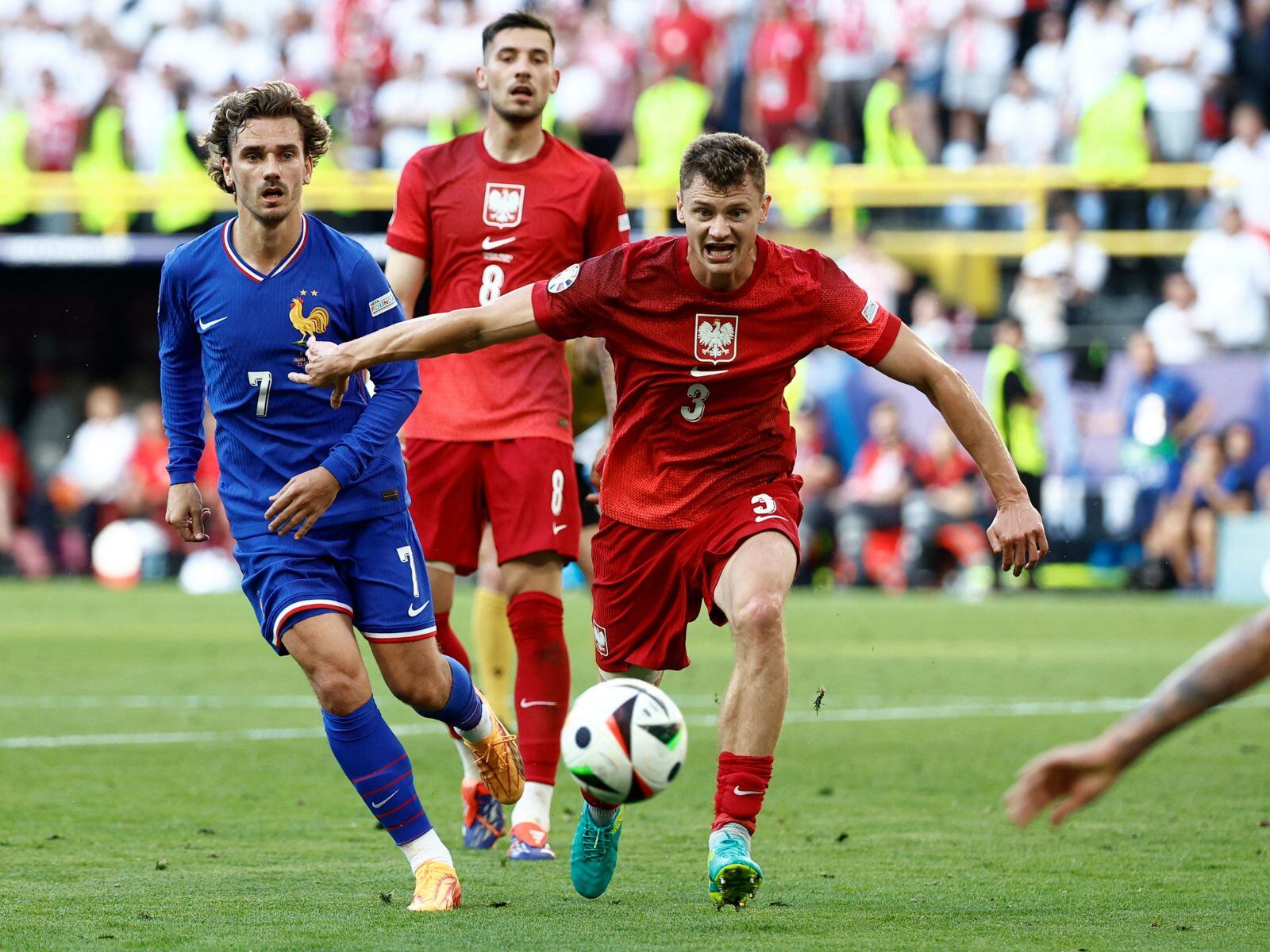 El centrocampista polaco #03 Pawel Dawidowicz (centro) lucha por el balón con el centrocampista francés #07 Antoine Griezmann (izq.) durante el partido de fútbol del Grupo D de la UEFA Euro 2024 entre Francia y Polonia en el BVB Stadion de Dortmund el 25 de junio de 2024. | Crédito: Kenzo Tribouillard / AFP