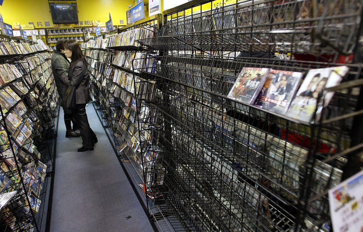 Los clientes miran videos junto a un estante casi vacío en una de las tiendas Blockbuster en Hong Kong, 30 de enero de 2004. (Foto de TED ALJIBE / AFP)