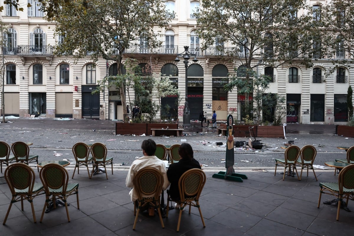 Dos clientes están sentados en la terraza de una cafetería, en una calle cubierta de escombros, un día después de las protestas a nivel nacional contra el «alto costo de la vida», en Marsella, el 18 de octubre de 2026. (Foto: Thibaud MORITZ / AFP)