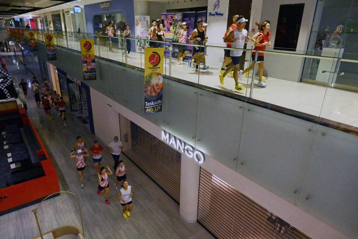 Aficionados al ejercicio físico corren dentro de un centro comercial debido a la bruma que afecta al exterior en Singapur, el 24 de octubre de 2026. (Foto de Roslan RAHMAN / AFP)
