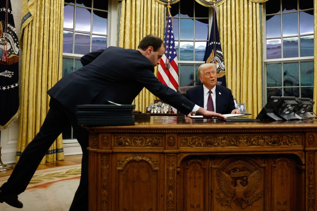 Un asistente le entrega al presidente Donald Trump una orden ejecutiva para firmar en la Oficina Oval de la Casa Blanca, el 20 de enero.