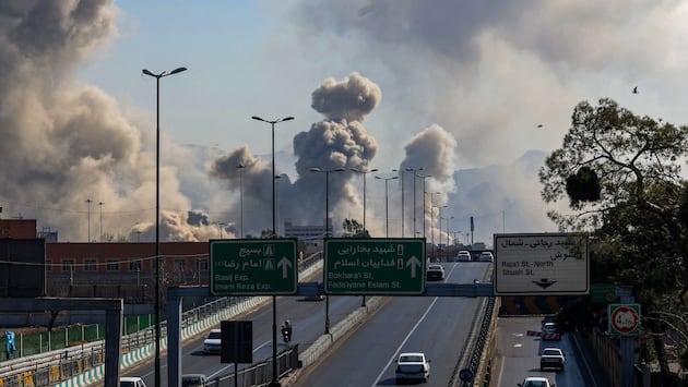 Automovilistas circulan por una autopista mientras columnas de humo se elevan tras un ataque en Teherán, Irán, el 5 de marzo de 2026. (Foto de ATTA KENARE / AFP).