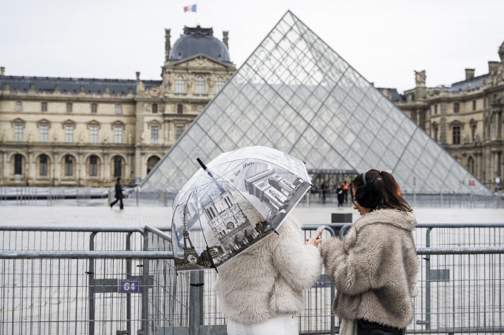 (ARCHIVOS) Turistas se paran junto a barreras que bloquean la plaza con la Pirámide del Louvre, diseñada por el arquitecto chino-estadounidense Ieoh Ming Pei, mientras el Museo del Louvre está cerrado debido a una huelga en París el 12 de enero de 2026. (Foto de Martin LELIEVRE / AFP)