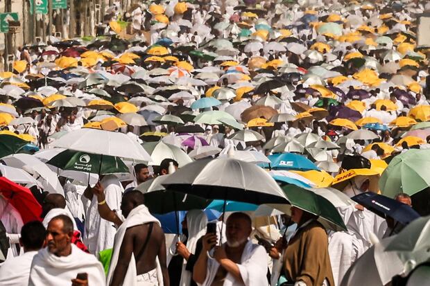 Muslim pilgrims use umbrellas to protect themselves from the sun as they arrive at the base of Mount Arafat, also known as Jabal al-Rahma or Mount of Mercy, during the annual haj pilgrimage on June 15, 2024. (Photo by Fadel SENNA / AFP)