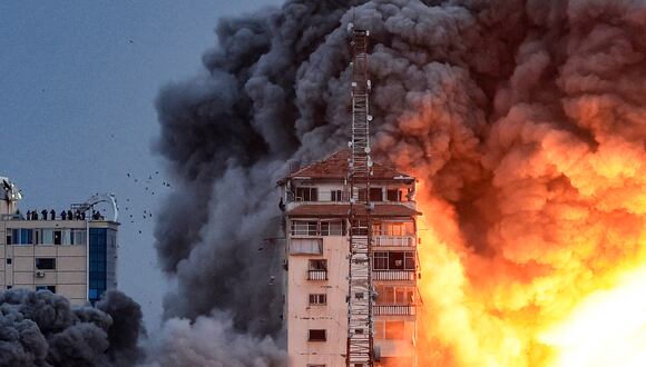 Personas paradas en una azotea observan cómo una bola de fuego y humo se eleva sobre un edificio en la ciudad de Gaza el 7 de octubre de 2023 durante un ataque aéreo israelí que golpeó el edificio de la Torre Palestina.(Foto de MAHMUD HAMS / AFP).