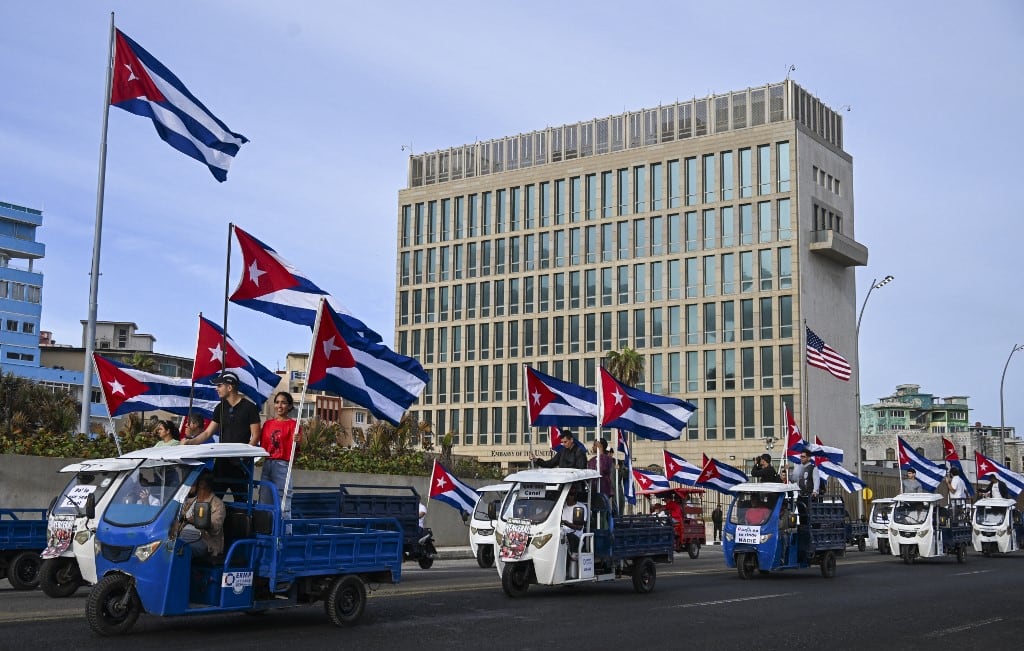 Cubanos en triciclos eléctricos decorados con banderas cubanas pasan frente a la embajada de Estados Unidos durante la marcha juvenil antiimperialista en La Habana el 2 de abril de 2026. (Foto de YAMIL LAGE / AFP)