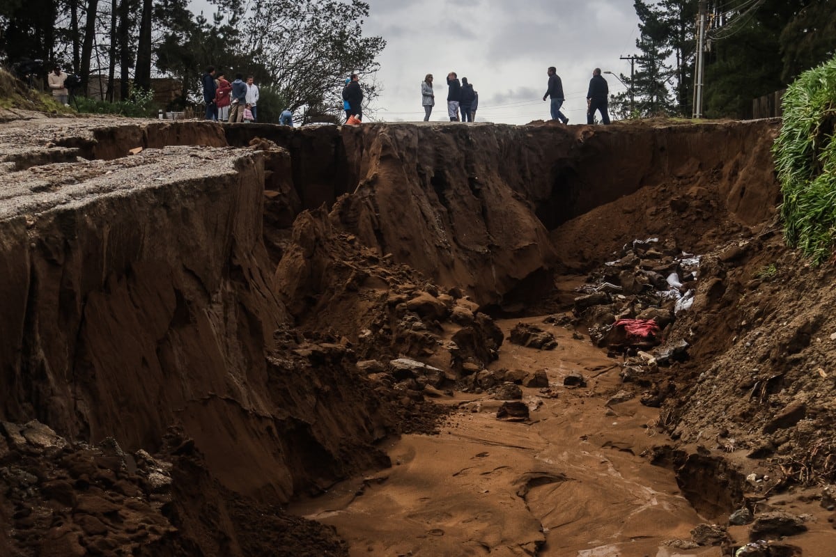 Varias personas se encuentran junto a un gran socavón formado tras las fuertes lluvias en Viña del Mar, Chile, el 18 de julio de 2026. (Cristobal Basaure / AFP)