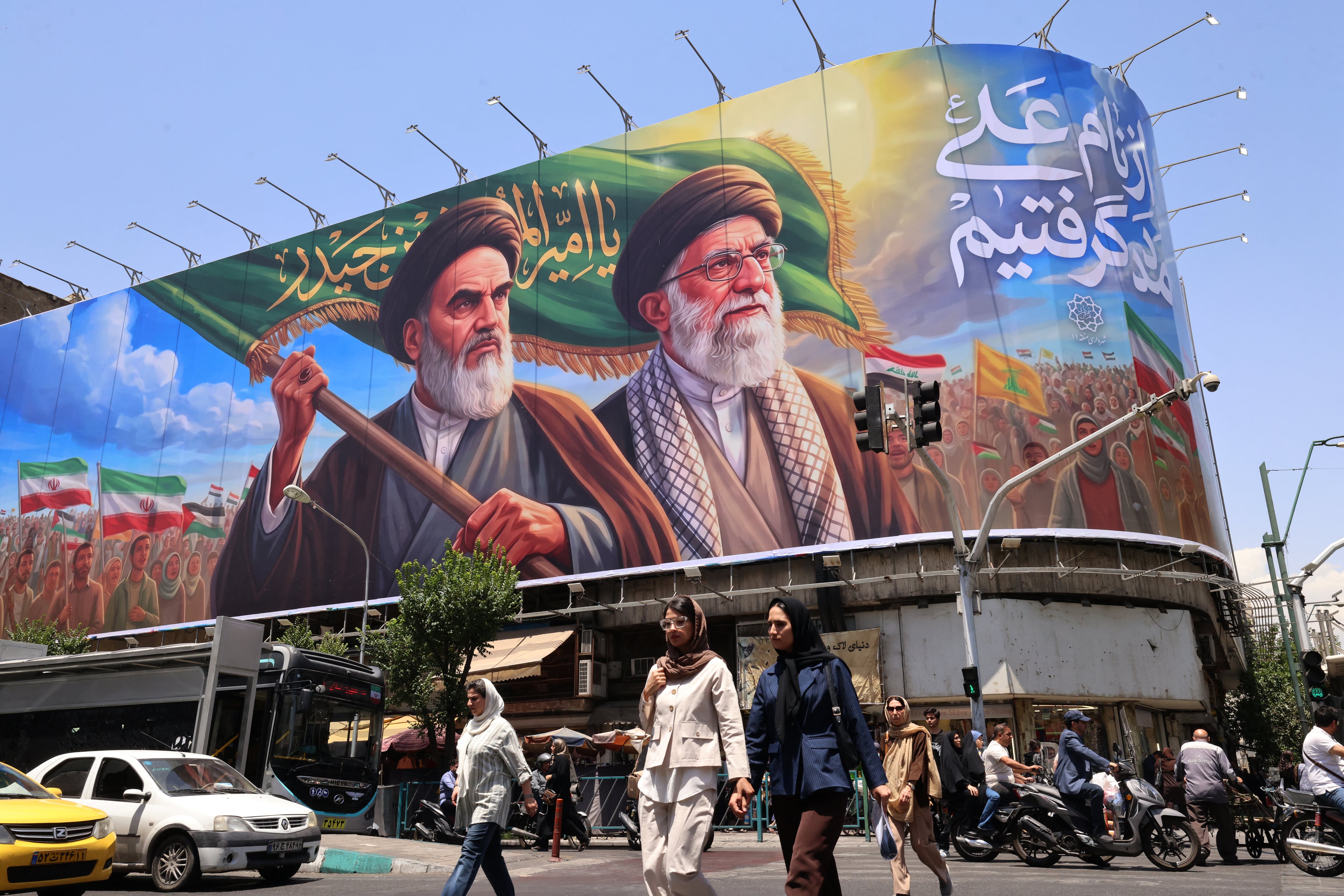 Varias personas cruzan la calle frente a una gran valla publicitaria que muestra retratos del difunto líder supremo de Irán, el ayatolá Ruhollah Jomeini (izquierda), y del líder supremo asesinado, el ayatolá Alí Jaamenei. (Foto de ATTA KENARE / AFP).