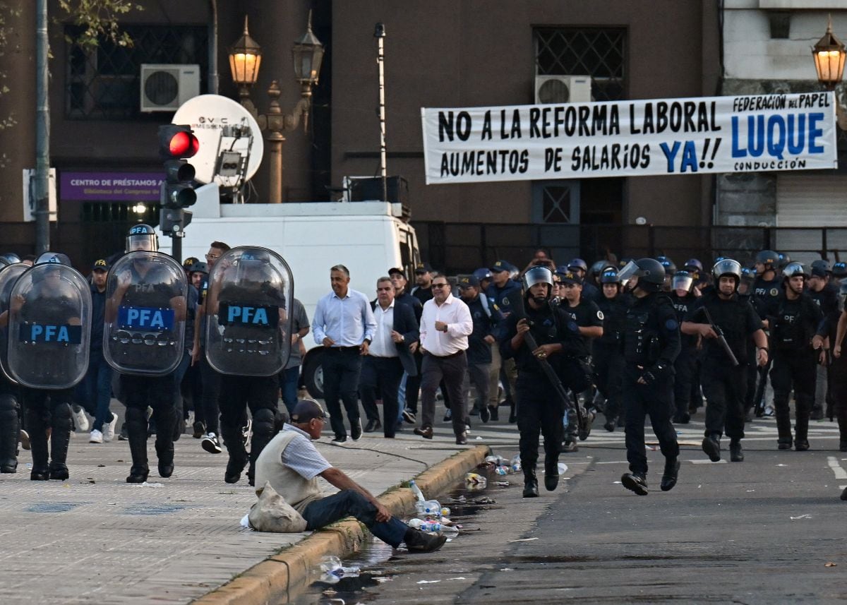 Un hombre se sienta en la acera mientras la policía toma posiciones durante una protesta frente al Congreso, donde se debate la reforma laboral del presidente argentino Javier Milei, en Buenos Aires el 19 de febrero de 2026 (Foto: Luis Robayo / AFP)