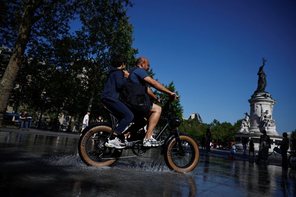 Two people cycle over a water puddle on Place de la Republique, central Paris on May 26, 2026 as a heatwave hits France. Western Europe faced another day of record-breaking temperatures Tuesday as a heatwave pushed the mercury well above normal levels for May. A so-called "heat dome" of warm air from northern Africa trapped under a high-pressure system over western Europe is behind the sort of heat not usually seen until high summer. (Photo by SIMON WOHLFAHRT / AFP)