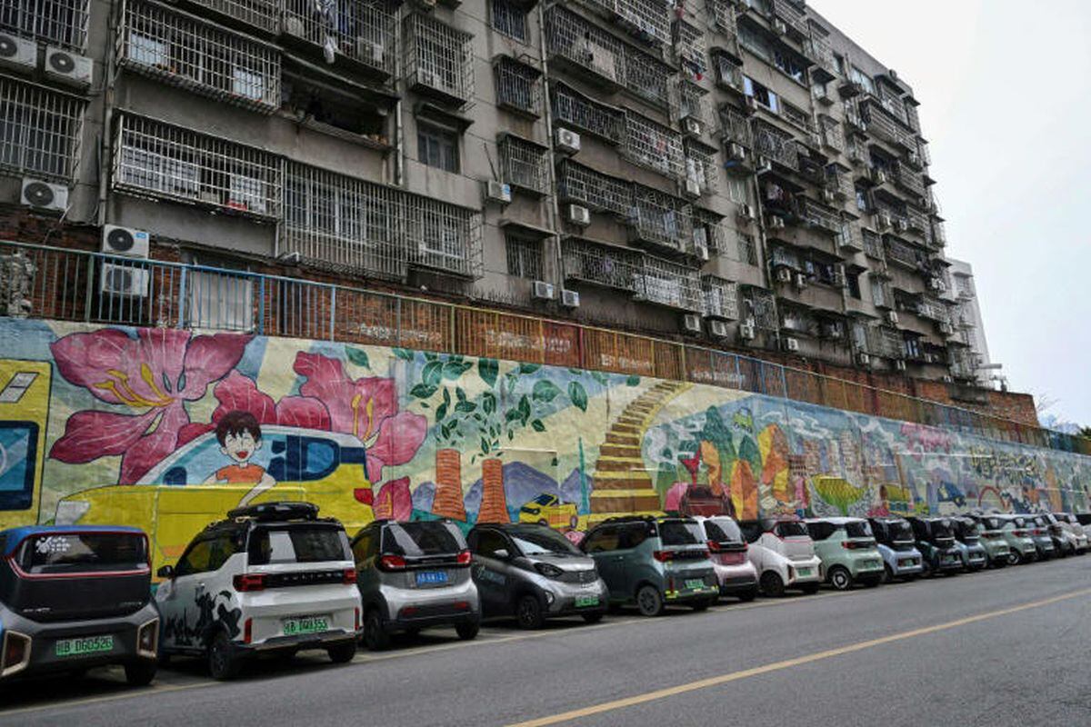 Miniautos eléctricos están estacionados en línea cerca de un mural junto a otros vehículos.(Foto: Jade GAO)
