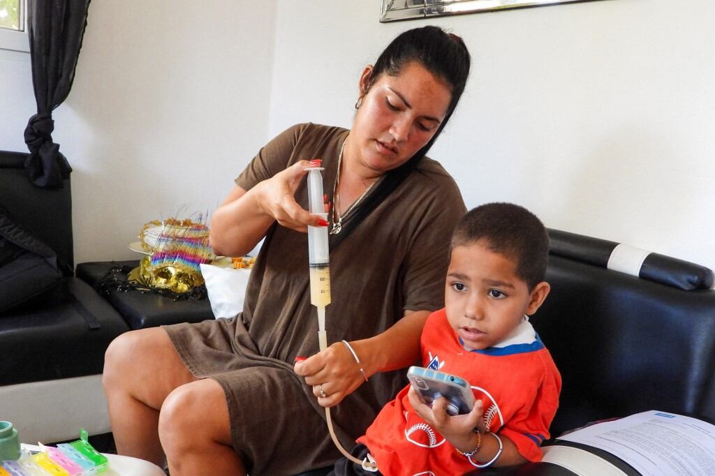 Jessica Rodríguez Romero administra medicamentos directamente en el estómago a su hijo Luis Ángelo, tras una traqueotomía, en su domicilio en el barrio de Santa Fe, La Habana, el 2 de julio de 2025. (Foto de ADALBERTO ROQUE / AFP)