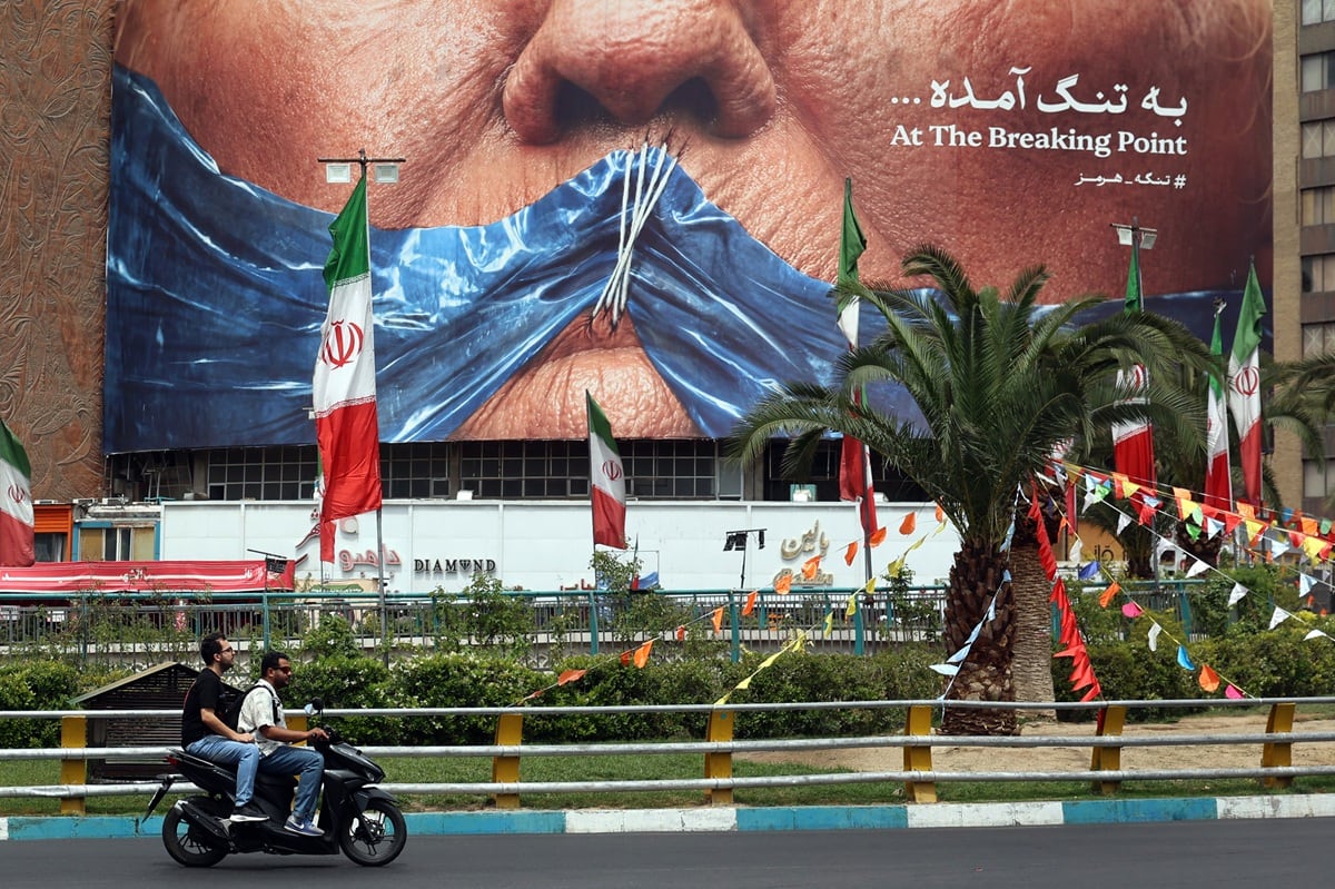 Iraníes pasean en motocicleta frente a una valla publicitaria que muestra al presidente estadounidense Donald Trump y el estrecho de Ormuz, erigida en la plaza Valiasr de Teherán, el 28 de mayo de 2026. (AFP)
