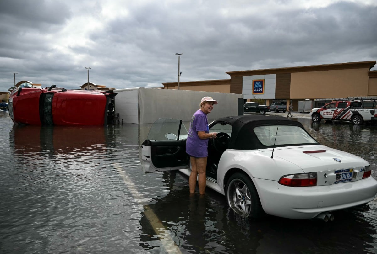 Una mujer inspecciona su coche en el aparcamiento inundado de un centro comercial en Tiger Point, Florida, el 10 de octubre de 2026. | Foto por RONALDO SCHEMIDT / AFP